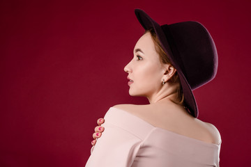 Beautiful young girl is standing in a hat on a red background