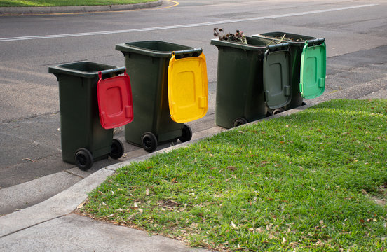 Australian garbage wheelie bins with colourful lids for recycling household waste and green garden waste lined up on the street kerbside for council rubbish collection