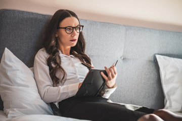 Businesswoman on business trip lying in hotel room and taking notes.