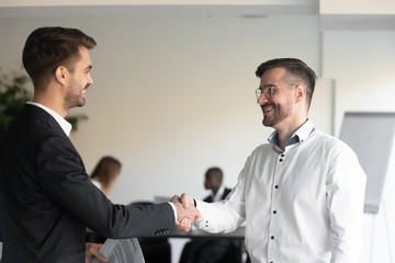 Two smiling business partners shaking hands with each other, celebrating good profitable deal. Happy executive getting acquainted to new corporate client. Hr manager welcoming new worker at office.