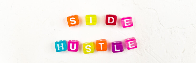 Side hustle phrase made of cube beads of different colors on white concrete background. Conxep of...