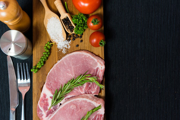 Top view raw pork chop meat on wood plate with vegetables, spices, salt and black pepper in dark black cloth table
