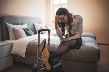 Tired businesswoman is sitting on bed in hotel.