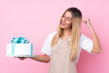 Young Uruguayan pastry woman with a big cake over isolated pink background celebrating a victory