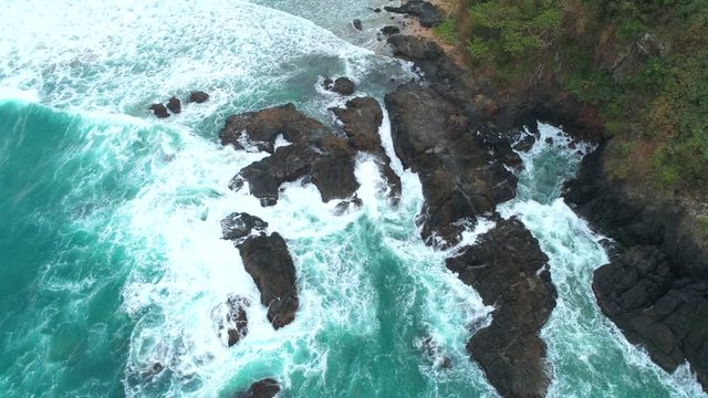 Aerial view of waves break on dark rocks near beach. Ocean waves crashing against rocky shore Palawan, Philippines