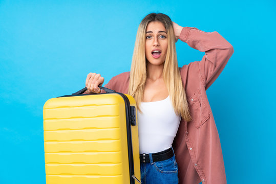 Young Uruguayan woman over isolated blue background in vacation with travel suitcase and surprised