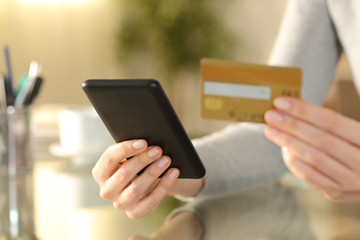 Woman holding phone and credit card on a desk at home