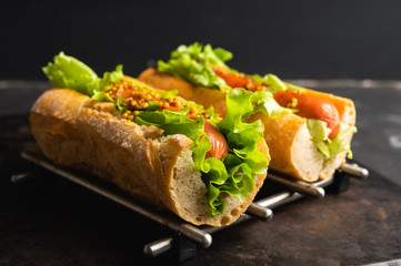 Tasty fresh hot dogs with grilled sausage, french mystard and fresh salad leaves on the rustic background. Selective focus. Shallow depth of field.