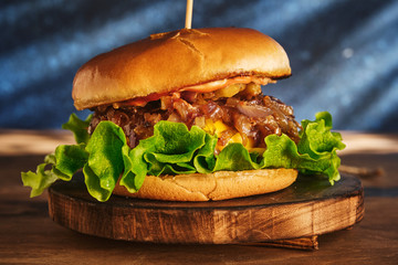 Burger with beef and caramelized onions on a wooden board. Cheeseburger with onion and beef. Juicy Delicious Homemade Burger.