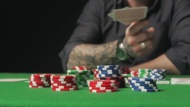 A man with tattoo winning game, grabbing all chips sitting at poker table