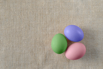 Three easter eggs on canvas surface. Colorful easter eggs decoration. Flat lay, top view. with copy space for text.