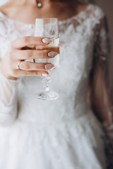 Closeup image of bride hand with perfect design manicure holding glass of fresh champagne. Bride morning. Female beauty and elegance.