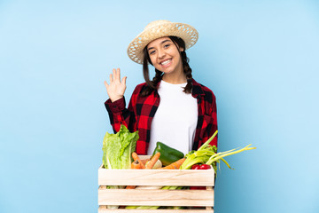 Young farmer Woman holding fresh vegetables in a wooden basket saluting with hand with happy expression