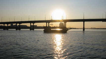 ship on the river against the background of the bridge and the setting sun