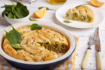 Delicious pie with spinach and feta cheese, made from filo pastry, decorated with sesame seeds. Traditional Greek pie spanakopita in a shape of roll.