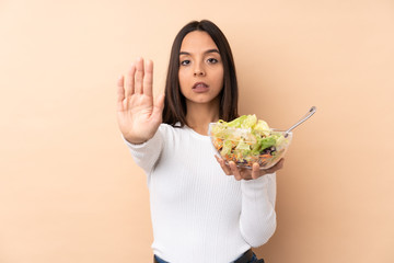 Young brunette girl holding a salad over isolated background making stop gesture and disappointed