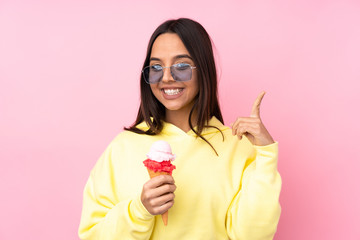 Young brunette girl holding a cornet ice cream over isolated pink background pointing up a great idea