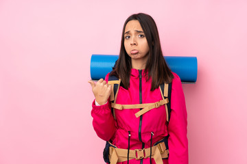 Young mountaineer girl with a big backpack over isolated pink background unhappy and pointing to the side