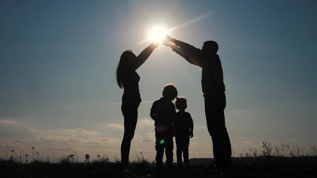 happy family teamwork silhouette shows a house and comfort symbol at sunset. mom dad and kids children portray a house roof hold their lifestyle hands over their heads
