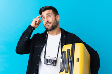 Traveler man holding a suitcase over isolated blue background having doubts and with confuse face expression