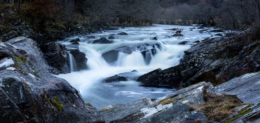 Naklejka na ściany i meble Long exposure shot of the waterfalls in Glen Orchy near Bridge of Orchy in the Argyll region of the highlands of Scotland during winter whilst the river is flowing fast from rainfall