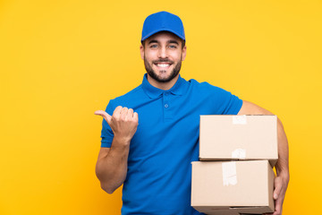 Delivery man over isolated yellow background pointing to the side to present a product