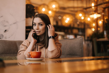 Young business woman in casual clothes sitting at table in cafe, talking on cell phone. On table cup of coffee. Freelancer working. Concept of leisure activity.