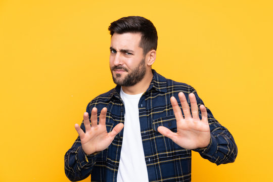 Young handsome man with beard over isolated yellow background nervous stretching hands to the front
