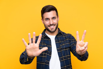 Young handsome man with beard over isolated yellow background counting seven with fingers - obrazy, fototapety, plakaty
