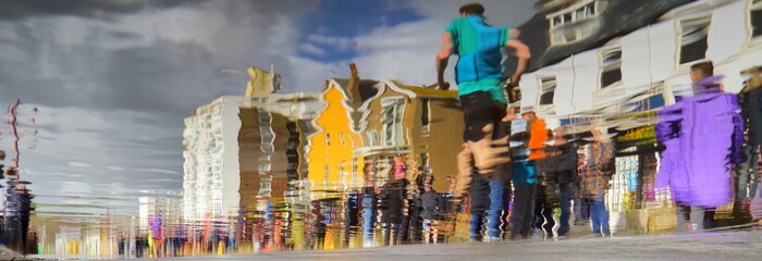 Blurred crowd on the street in Seaton, Devon reflected in water surface
