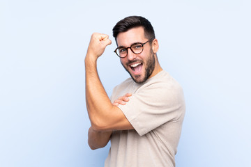 Young handsome man with beard over isolated blue background making strong gesture