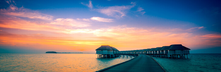 Fototapeta na wymiar Amazing sunset panorama at Maldives. Luxury resort villas seascape with soft led lights under colorful sky. Beautiful twilight sky and colorful clouds. Beautiful beach background for vacation holiday