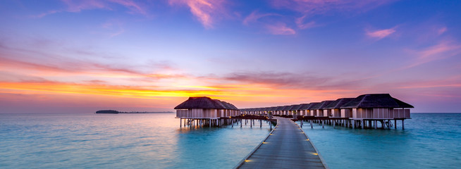 Amazing sunset panorama at Maldives. Luxury resort villas seascape with soft led lights under...