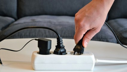 Three different electrical plugs connected to a power strip or extension block. Electric plugs with Multi-socket power strip, panoramic view. Male hand connecting an electrical plug to a power strip