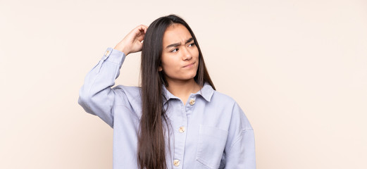 Young Indian woman isolated on beige background having doubts while scratching head