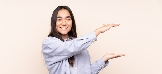 Young Indian woman isolated on beige background holding copyspace to insert an ad