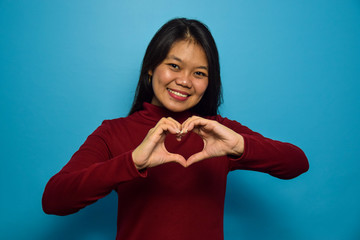 Portrait of Young beautiful asian women with blue isolated background, Make love with hands, Love Gesture