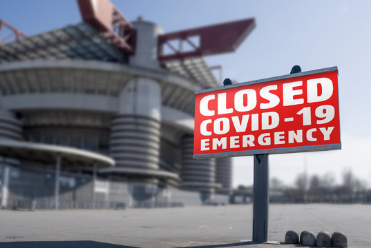 Red warning sign for Covid-19 in front of closed stadium. Concept of cancellation of sporting events due to corona virus medical emergency. Purposely blurred stadium in the background.