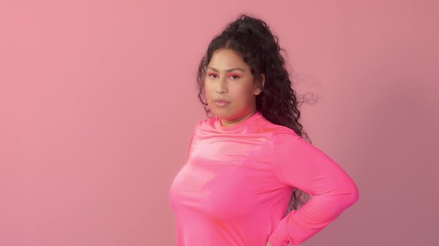 Young plus size mixed race woman with curly hair wears a bright neon makeup with curly hair blowing. No beauty norms concept