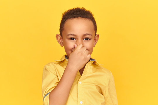 Odor, Bad Smell, Disgust And Body Scent Concept. Disgusted Displeased Dark Skinned Boy Pinching Nose With Fingers, Holding Breathe Because Of Unpleasant Gross Stink From Sweaty Armpits Or Dirty Socks