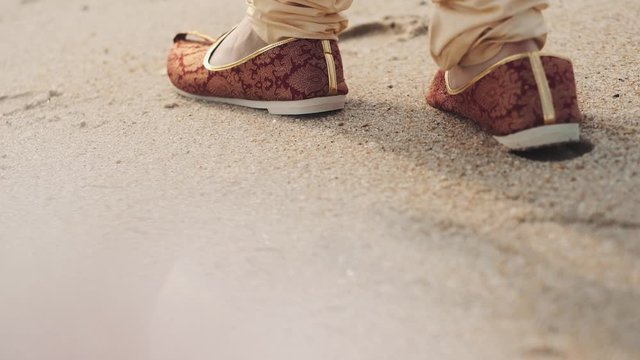 Indian man weared in the traditional shoes mojari is walking on the beach, close up, without face