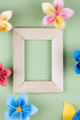 multi-colored paper flowers around wooden frame on green background.
