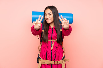 Young mountaineer Indian girl with a big backpack isolated on pink background smiling and showing victory sign