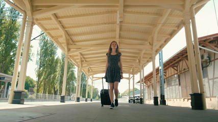 Obraz premium Young Slender Woman is Traveling and Walking on Vintage Train Station with Suitcase
