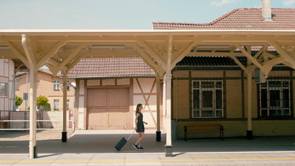 Slender Woman with Luggage is at the Beautiful Train Station in a Small Town Departing to Holiday Journey in Summer