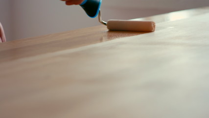 Close Up Shot of Man Hands Finishing and Oiling Wooden Desk Table with Roller with Oil or Varnish Indoors