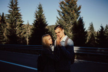 Happy, joyful, young couple on a walk in a pine forest on a sunny autumn day. Warm day sun light on faces lovely couple. Happy young couple hugging hands with amazing pine forest view. 