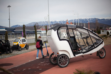 Bike for walks in the park. Car at the rickshaw. Tricycle mechanical vehicle. Transport for tourists in the park. The bike is parked. White indoor car.