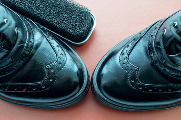 A Shoe sponge next to polished black leather shoes on an orange background with space for text.