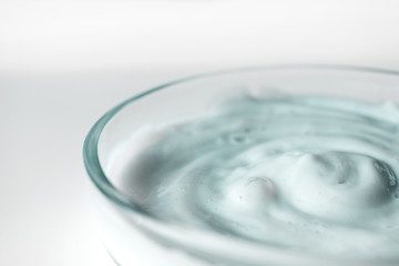 Facial scrub texture in glass container with selective focus, close-up. Cosmetic body and hair care product on white background